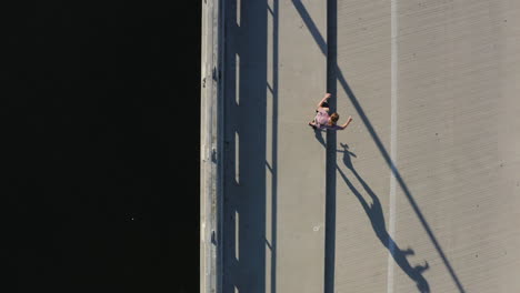 person skateboarding on coastal asphalt sideway and road, top down aerial view