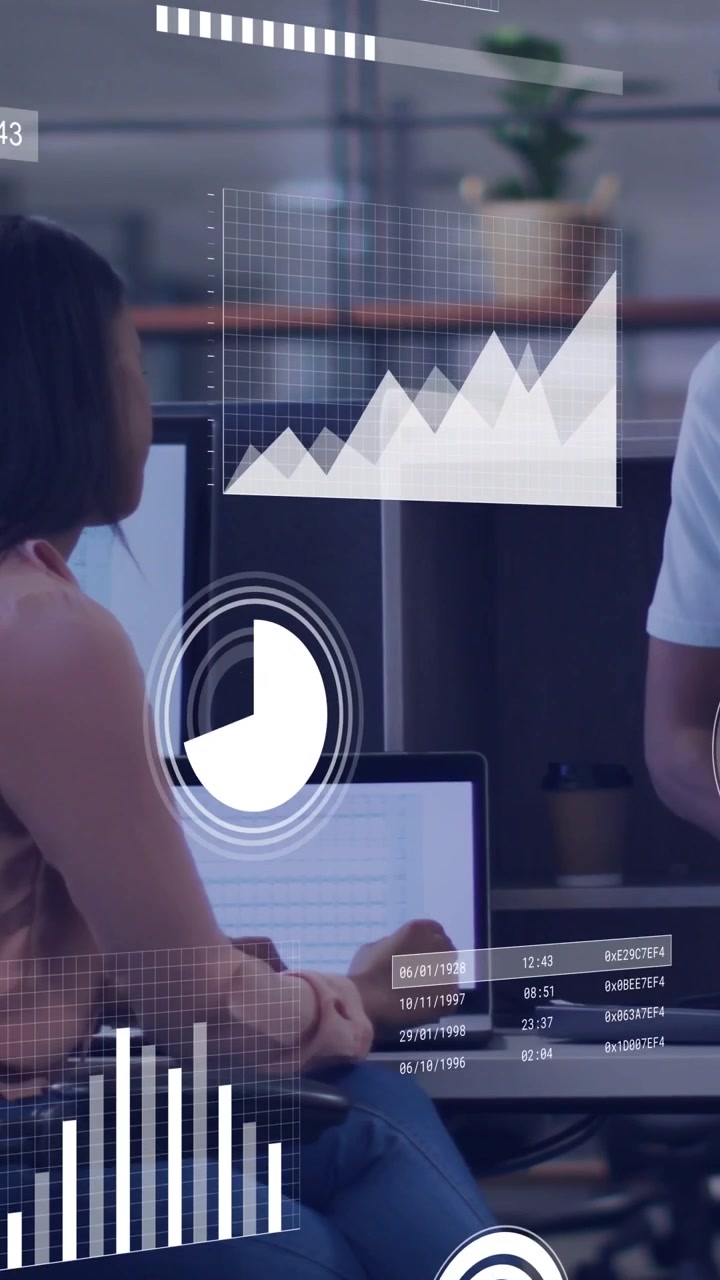 Vertical video: Seated woman pointing at monitor, standing man analyzing data with moving charts