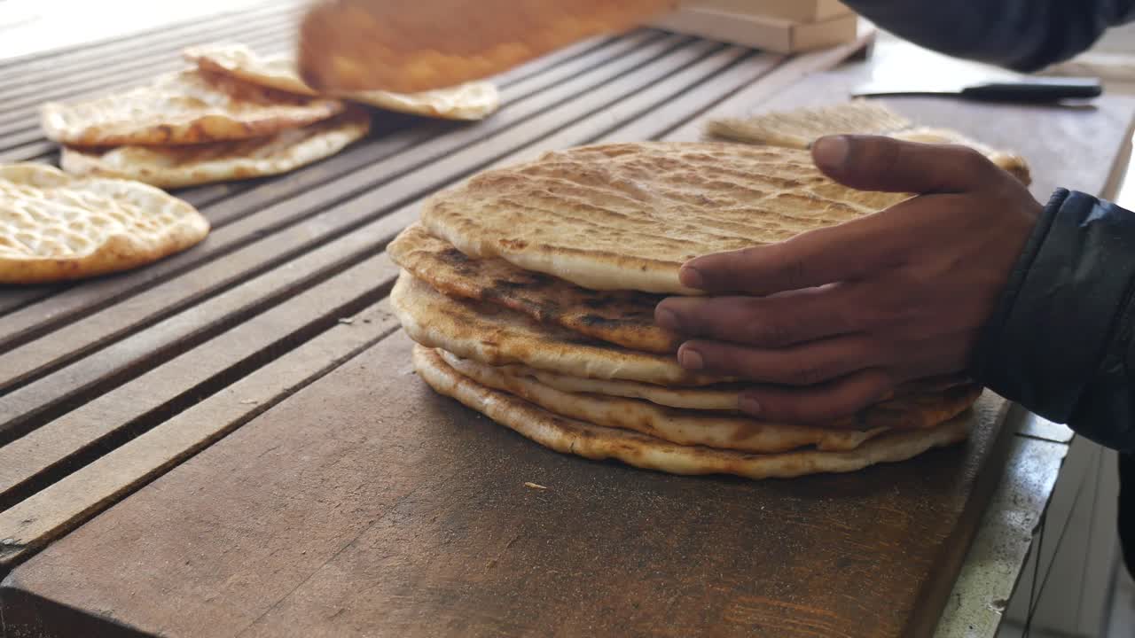 Hands Stacking Freshly Baked Traditional Flatbread on a Wooden Surface