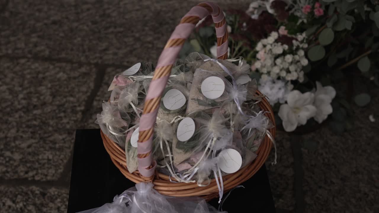 basket of organza wedding cones with flower petals rests near floral arch on stone path