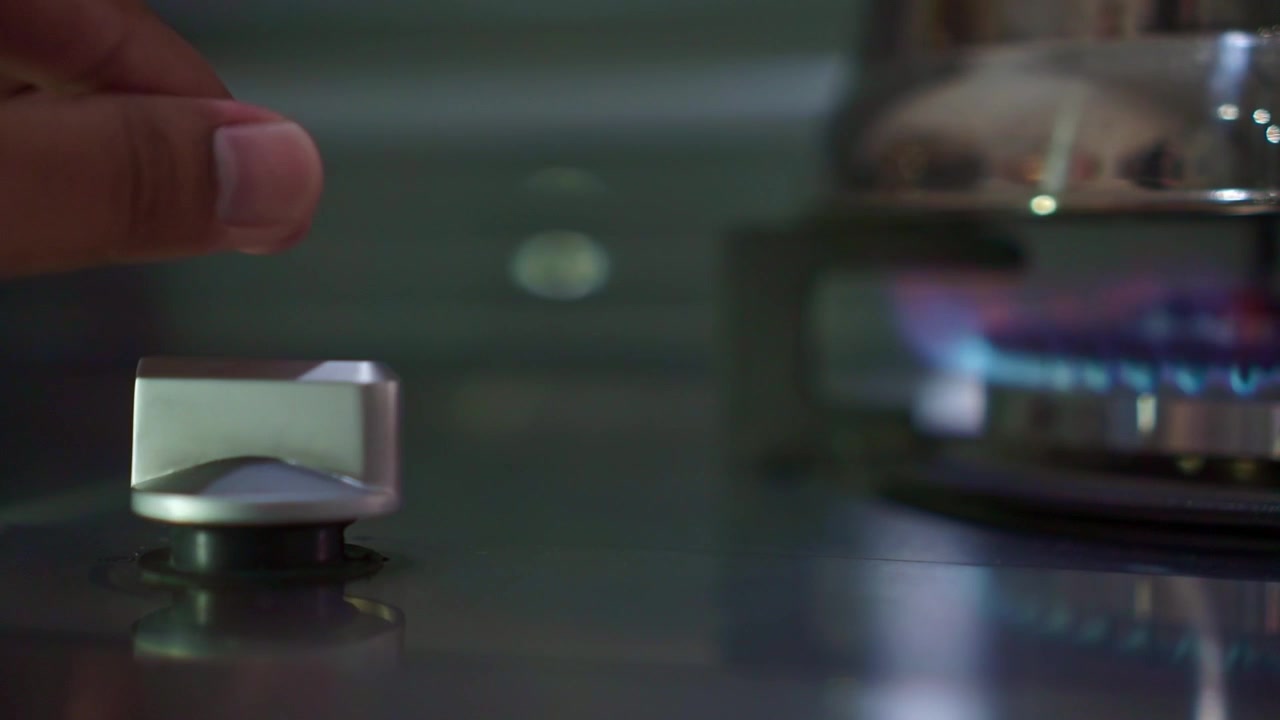 Person's fingers adjusting gas cooktop knob to start burner flame. Home kitchen appliance, cooking preparation, lifestyle stock footage.