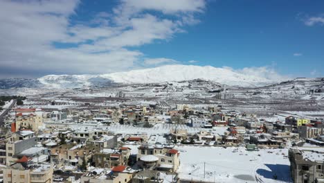 casas y campos cubiertos de nieve mientras las sombras se mueven lentamente sobre la montaña hermon en el fondo