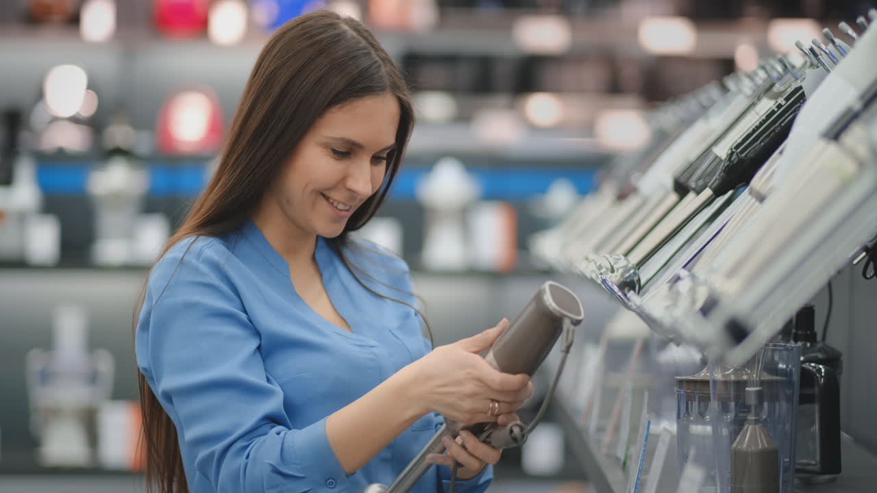 una joven hermosa con camisa azul elige una licuadora en una tienda de electrodomésticos