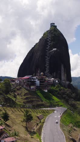 towering rock formation with a stairway, surrounded by scenic colombian landscape. aerial, vertical video