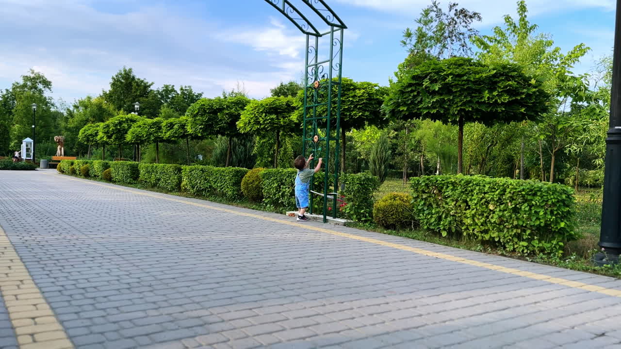 Caucasian toddler wearing jeans romper walking outdoors. Baby boy spending time in the park in summer.