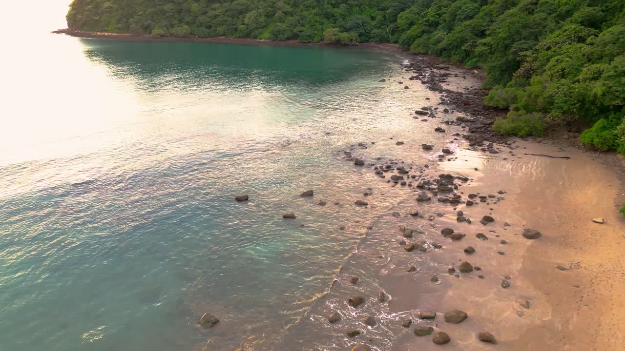 vista aérea de drones de la playa con árboles y rocas, aguas azules claras durante la puesta de sol