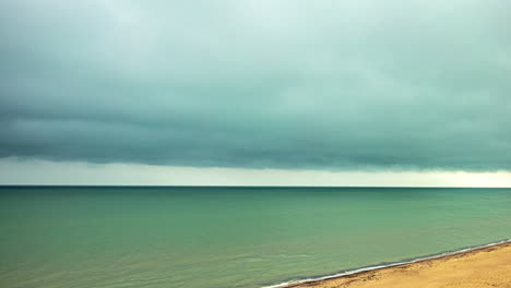 Zeitrafferaufnahme-Einer-Dunklen-Wolke,-Die-Sich-An-Einem-Regnerischen-Tag-über-Den-Sandstrand-Bewegt-Und-Meereswellen-Kracht