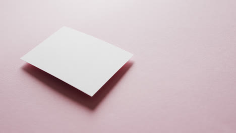 Close-up-of-blank-white-business-card-on-pink-background,-copy-space,-slow-motion