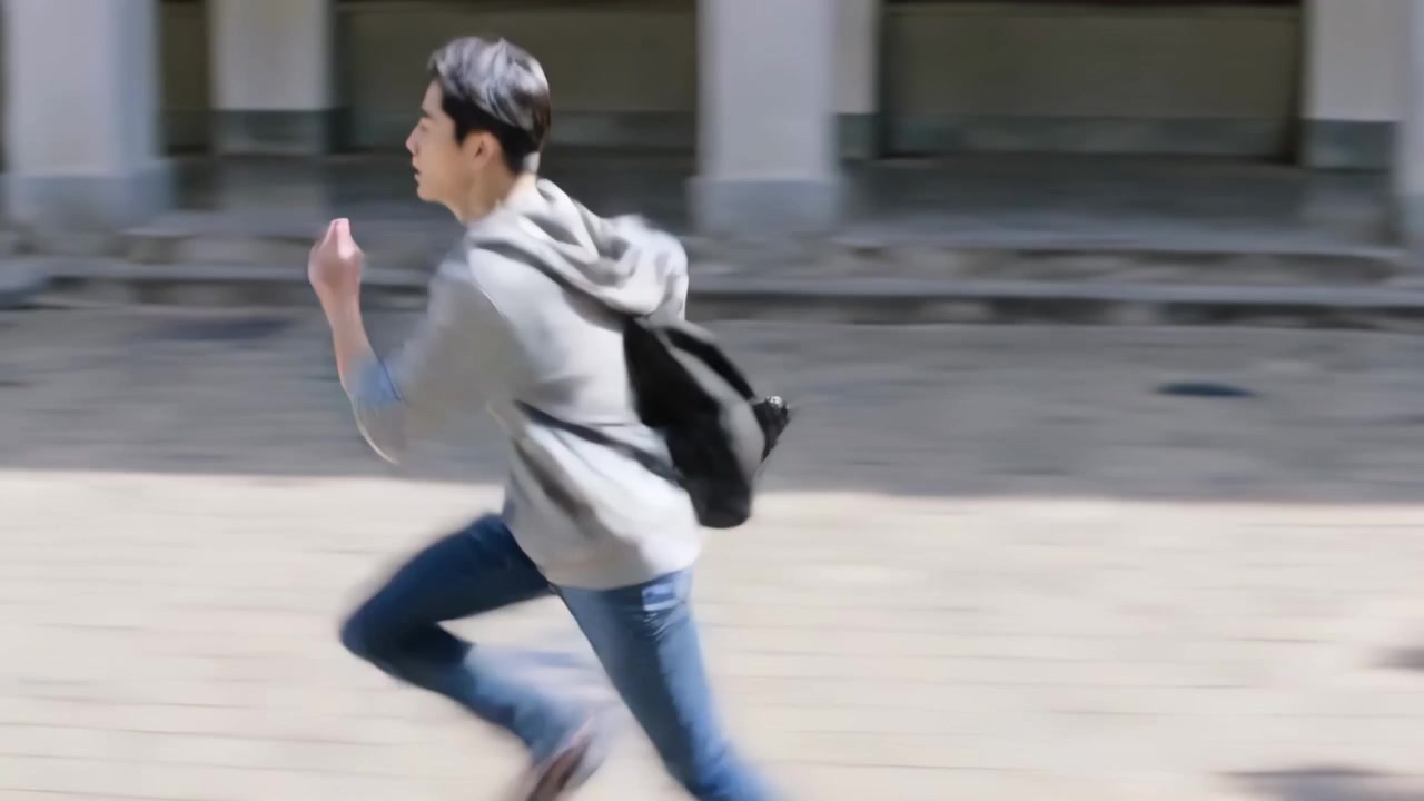 Sprinting male student charging across paved campus courtyard, carrying black backpack, grey hoodie