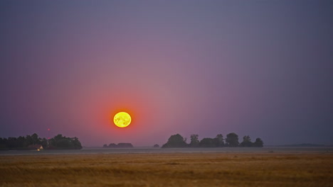 Ultra-bright-full-moon-setting-down-behind-rural-landscape,-time-lapse