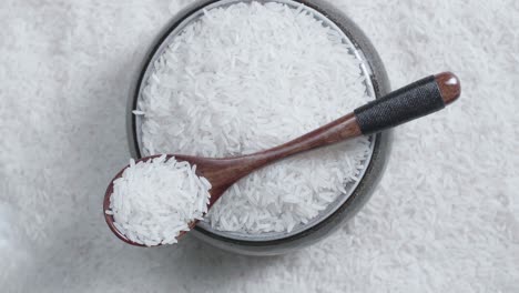 raw rice grain in the bowl and spoon rotate in slow motion. white rice grains food background