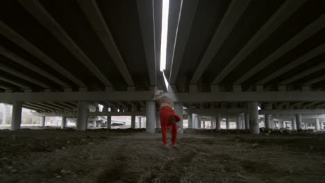 young traceur doing parkour stunts under urban bridge