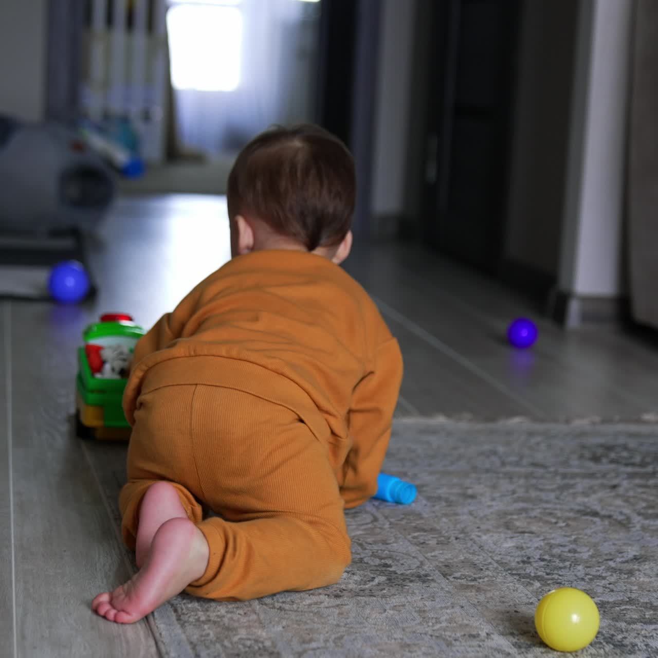 Toddler boy plays in the room. Little cute child crawls by the floor with scattered toys around. Sweet kid pushing the car