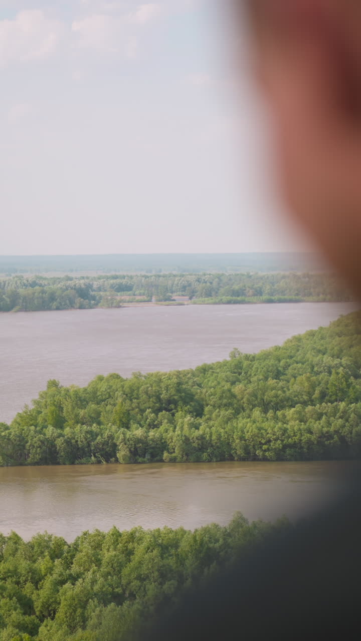Blurry person enjoys inspiring landscape view with wide tranquil river and boundless green forest on bank on sunny day extreme closeup slow motion