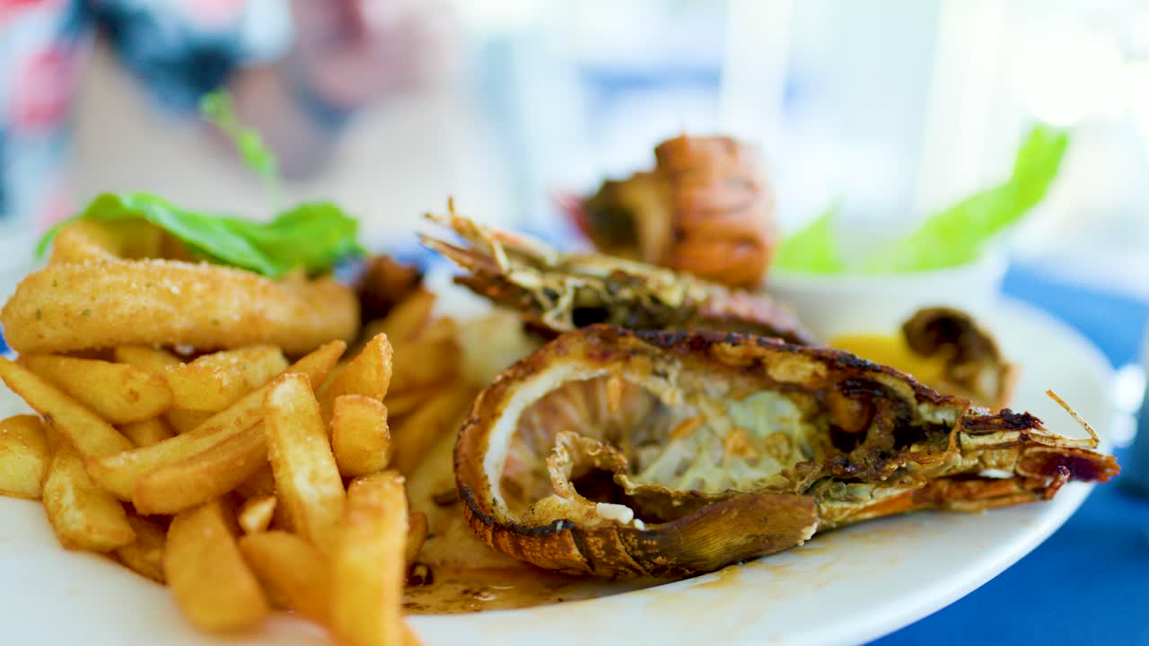 Close-up of fresh seafood platter with grilled lobster, fries, and garnish in bright restaurant lighting
