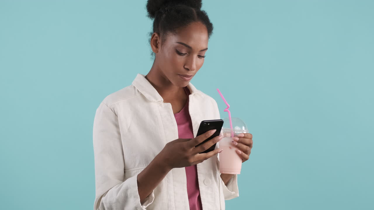 Smiling woman drinking milkshake and using phone