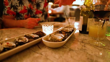 A person selects oysters from a platter in a dimly lit restaurant setting, capturing a casual dining experience