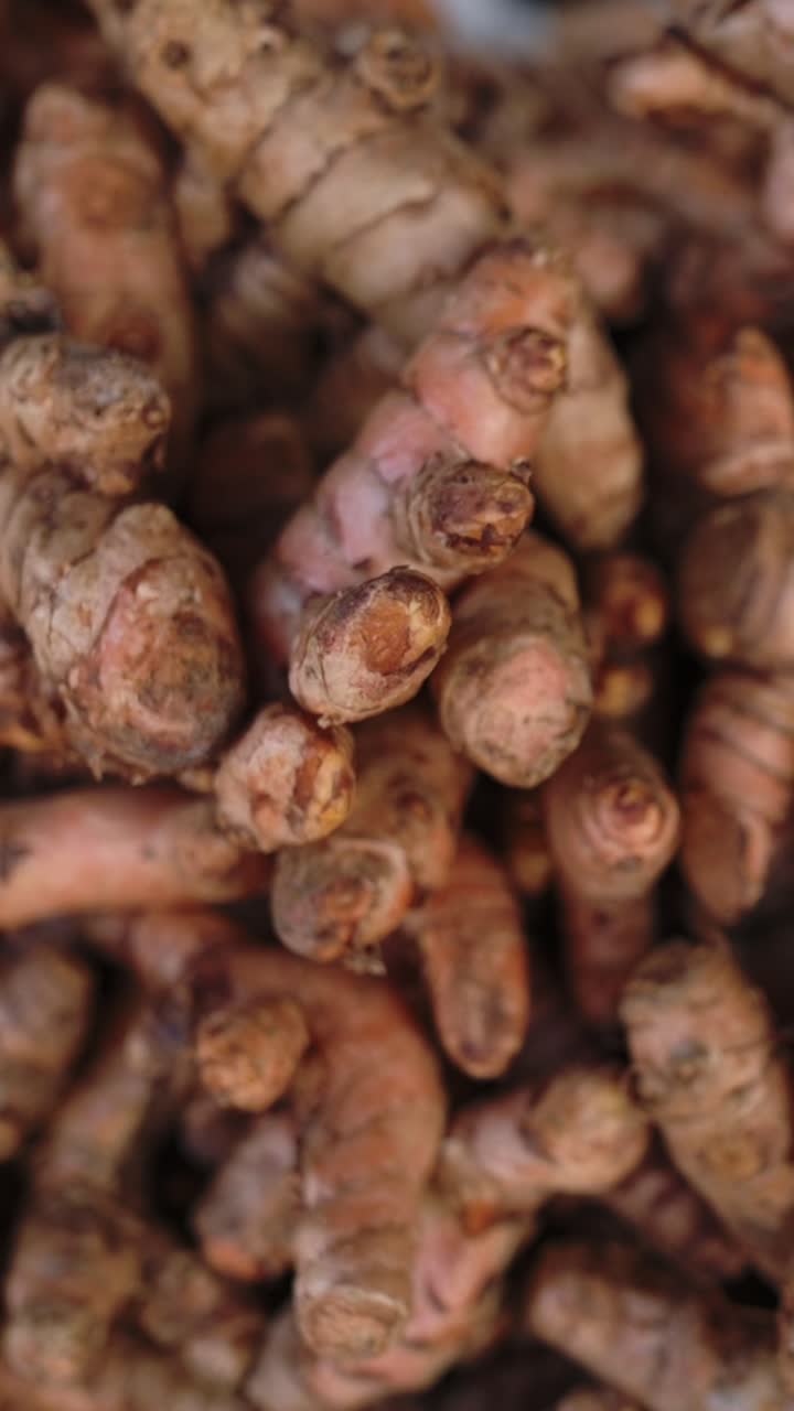 Schermo verticale: Radici di curcuma terrose ammassate in un mercato di strada vietnamita. Rizomi nodulosi marrone-arancio con tracce di terra, creando un'atmosfera speziata e aromatica. Casse rustiche, con un fascino erboristico e culinario, ideale