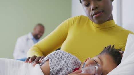 african american mother with patient son in oxygen mask, lying in bed at hospital