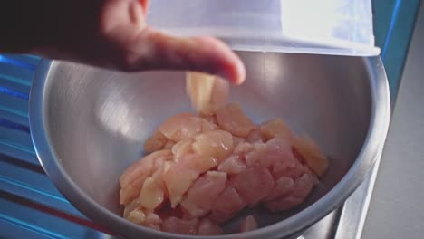 tirando trozos de pollo crudo en un arco en la cocina de casa