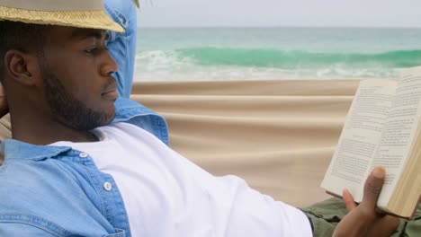 side view of african american man reading a book on the beach 4k