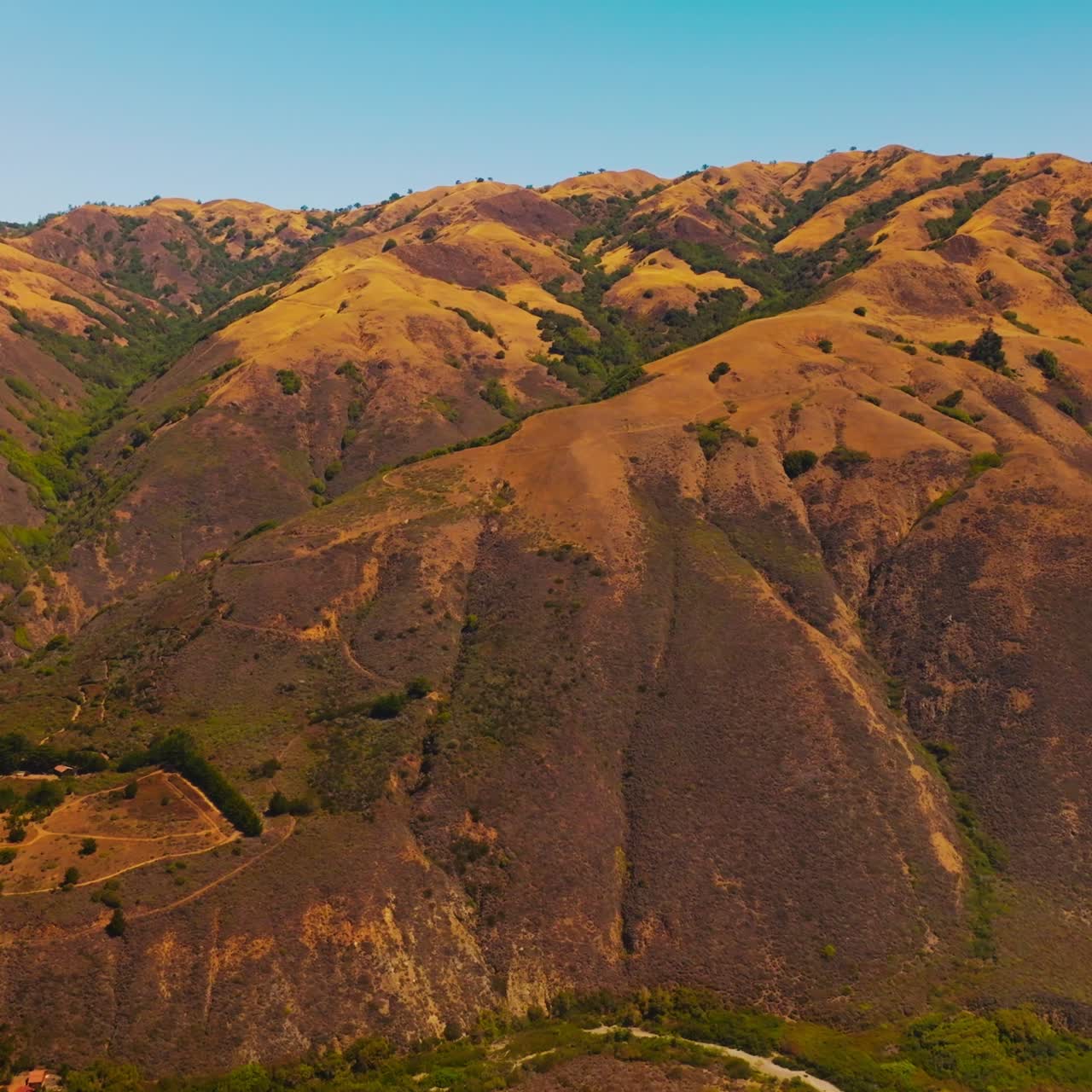 Approaching the sloping bare mountains with scarce vegetation at the foot. Beautiful rocky landscape at the backdrop of clear blue skies