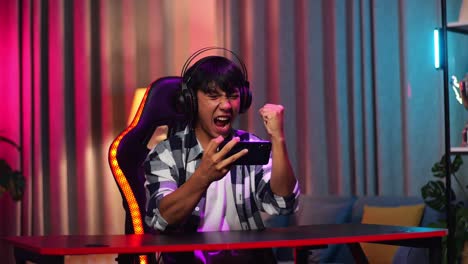 excited asian teen boy gamer celebrates victory and dancing while playing video game on smartphone