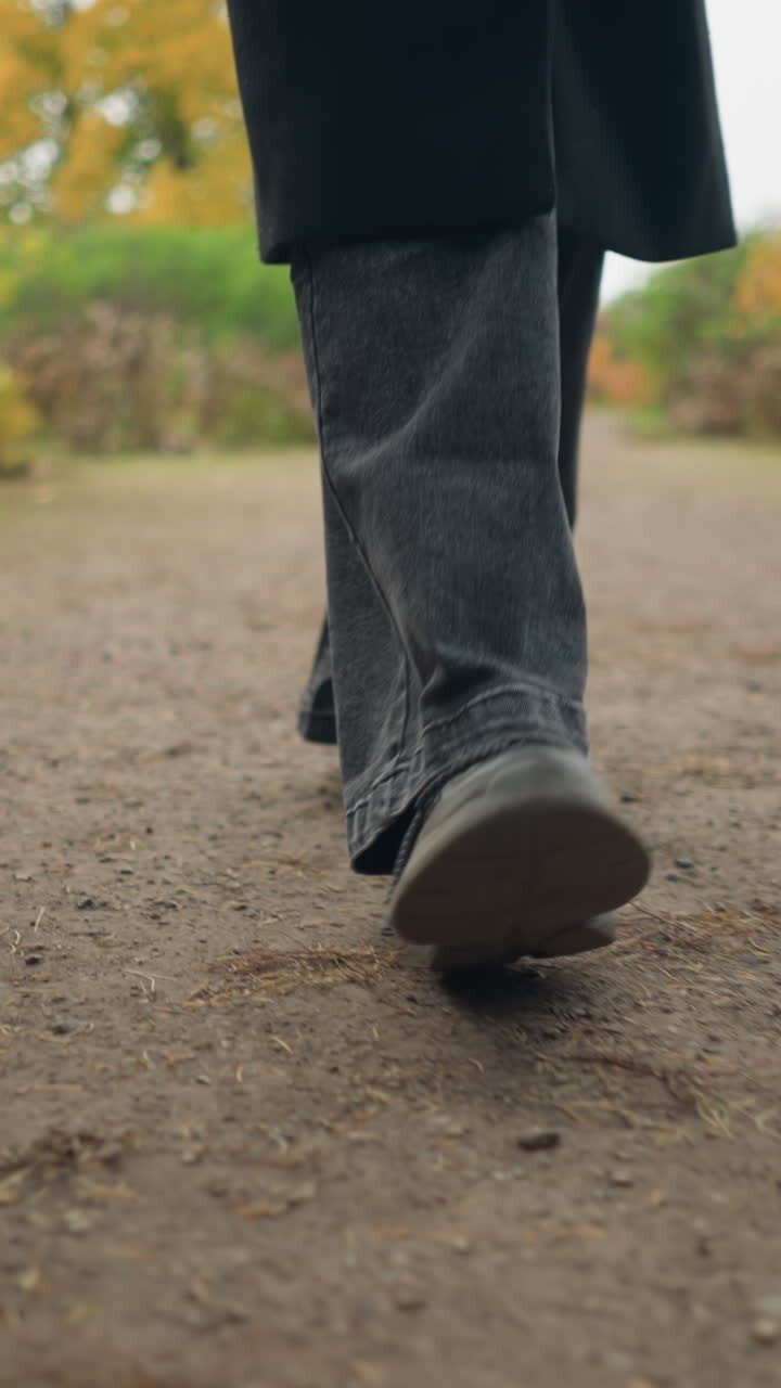 Close-up of feet in motion black jeans and canvas shoes jogging through a colorful autumn garden, capturing the essence of an active outdoor lifestyle amid fall scenery