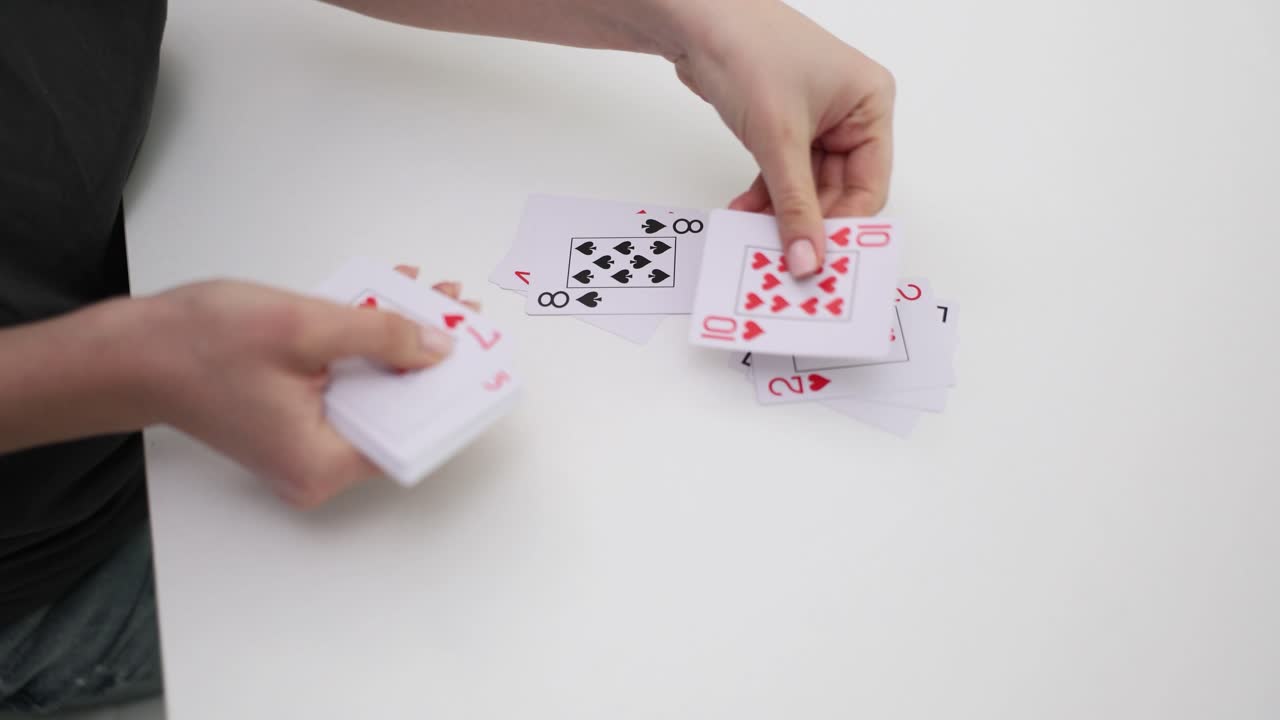 Nærbillede af hænder, der sorterer og arrangerer spillekort på et hvidt bord