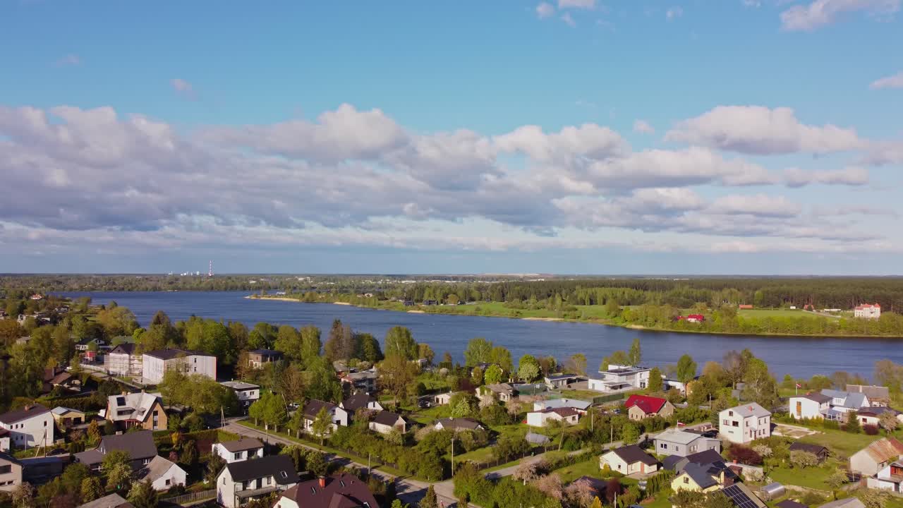Aerial of quiet suburb in spring with homes, trees, and roadways under blue sky, establishing pullback along from river