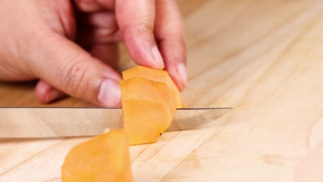 hands skillfully slice an orange fruit into small pieces on a wooden surface.