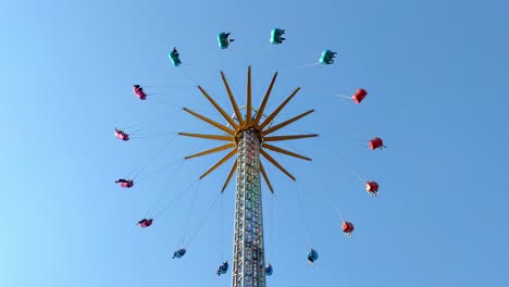 vertical colorful chain fair swing spinning people around, symmetrical minimal background blue sky, static