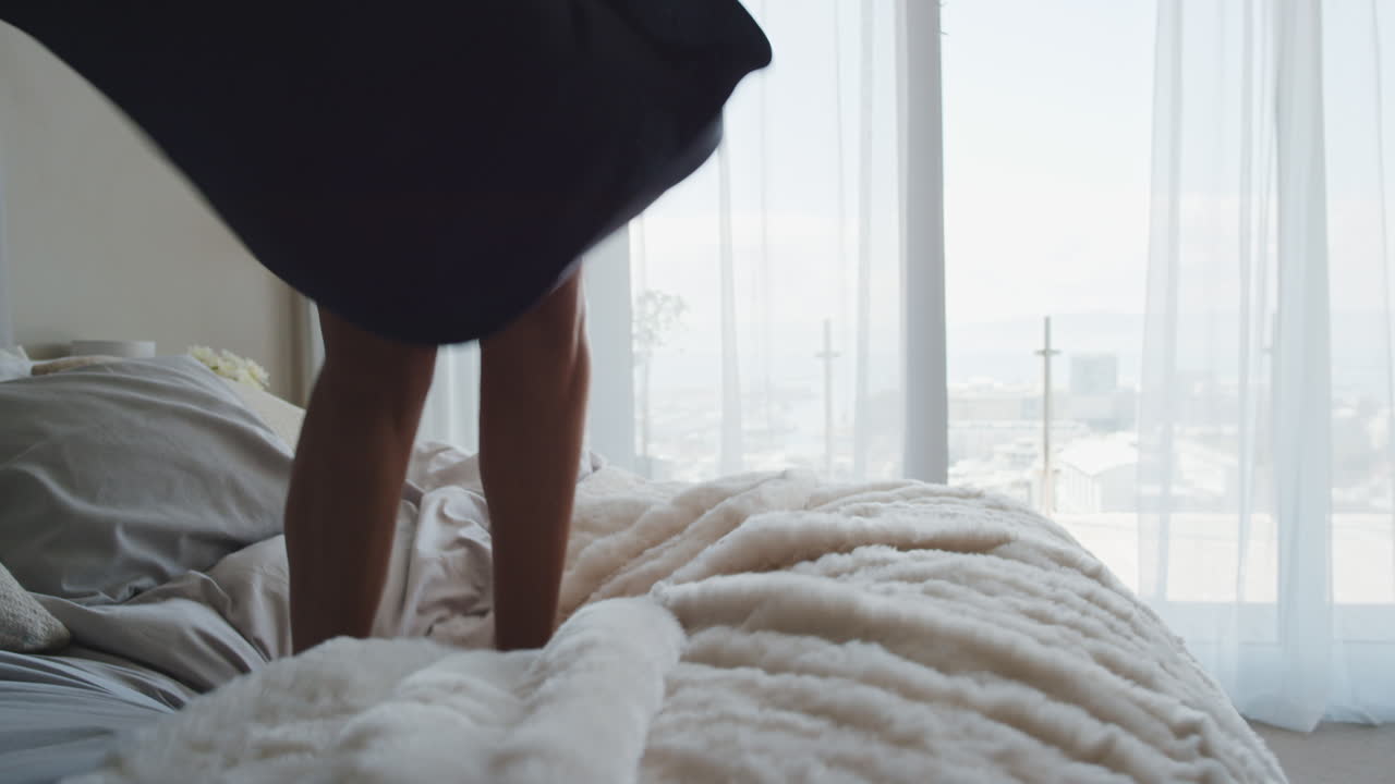 행복한 여성이 호텔 방에서 침대에 뛰어들어 즐거운 성공적인 라이프 스타일을 축하하고 럭셔리 펜트하우스 아파트를 즐기고 있습니다.