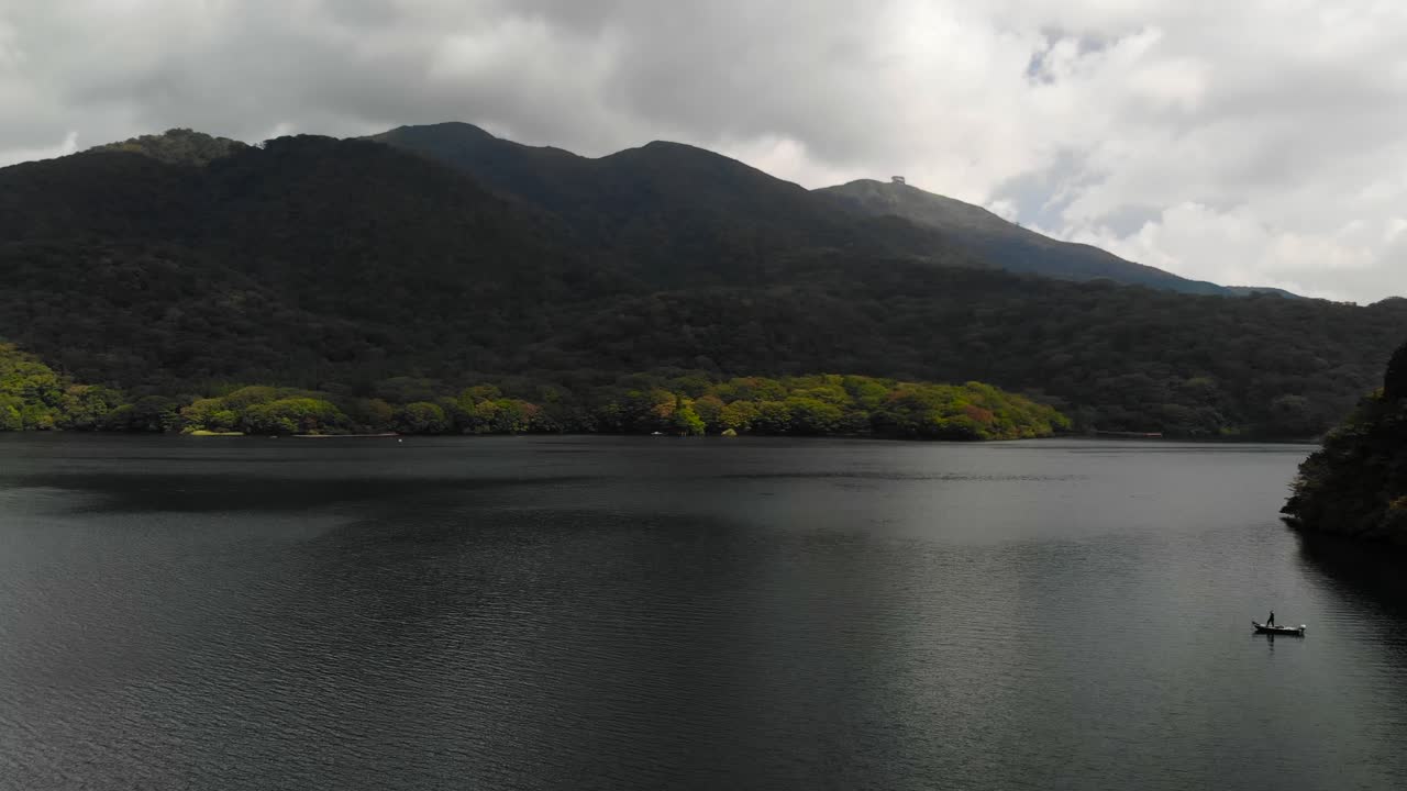 푸른 언덕을 배경으로 넓은 호수에서 낚시 보트에 서있는 사람과 공중으로 날아가는 드론 샷