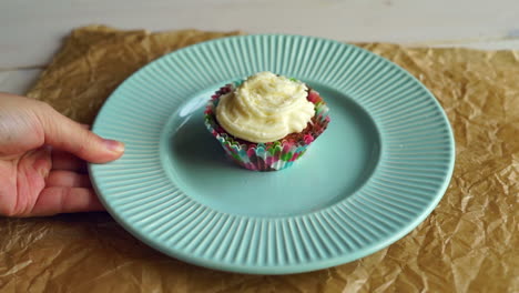 Hand-put-dessert-plate-with-cupcake-on-table.-Vanilla-cupcake-with-cake-cream