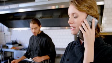 Female-chef-looking-at-clipboard-while-talking-on-phone-4k