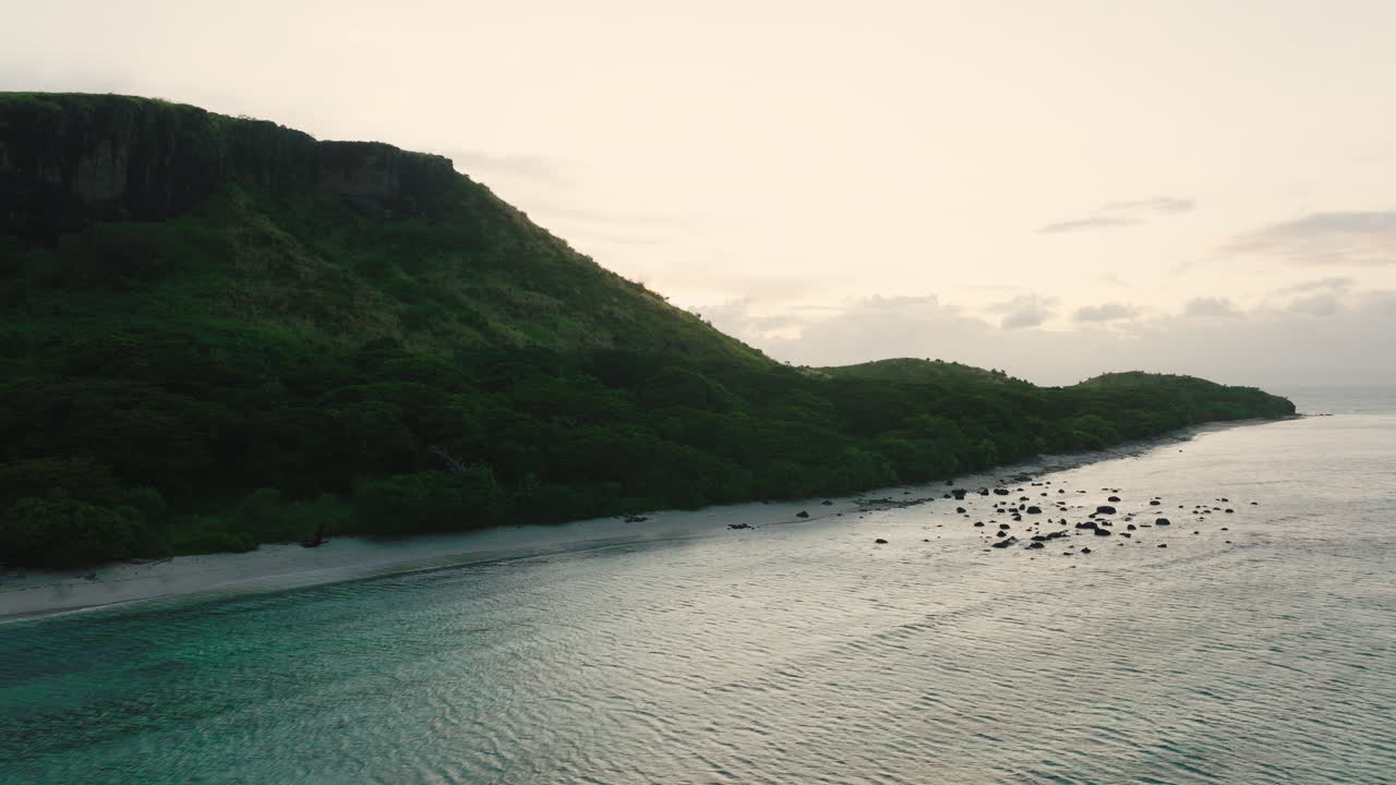Tropical coastline at sunset with hazy light and silhouetted hill in the distance