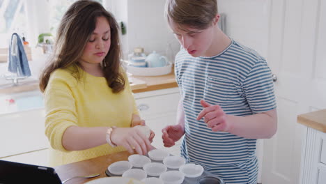 young downs syndrome couple putting paper cupcake cases into tray in kitchen at home