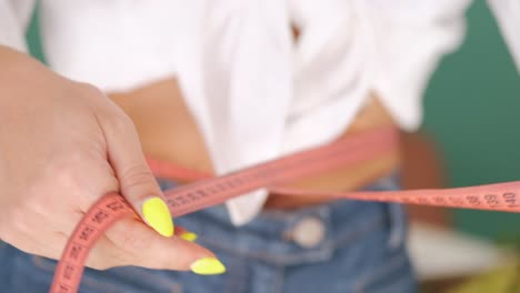 close up of woman while happily measuring her waist, using clothing measuring tape, weight loss concept