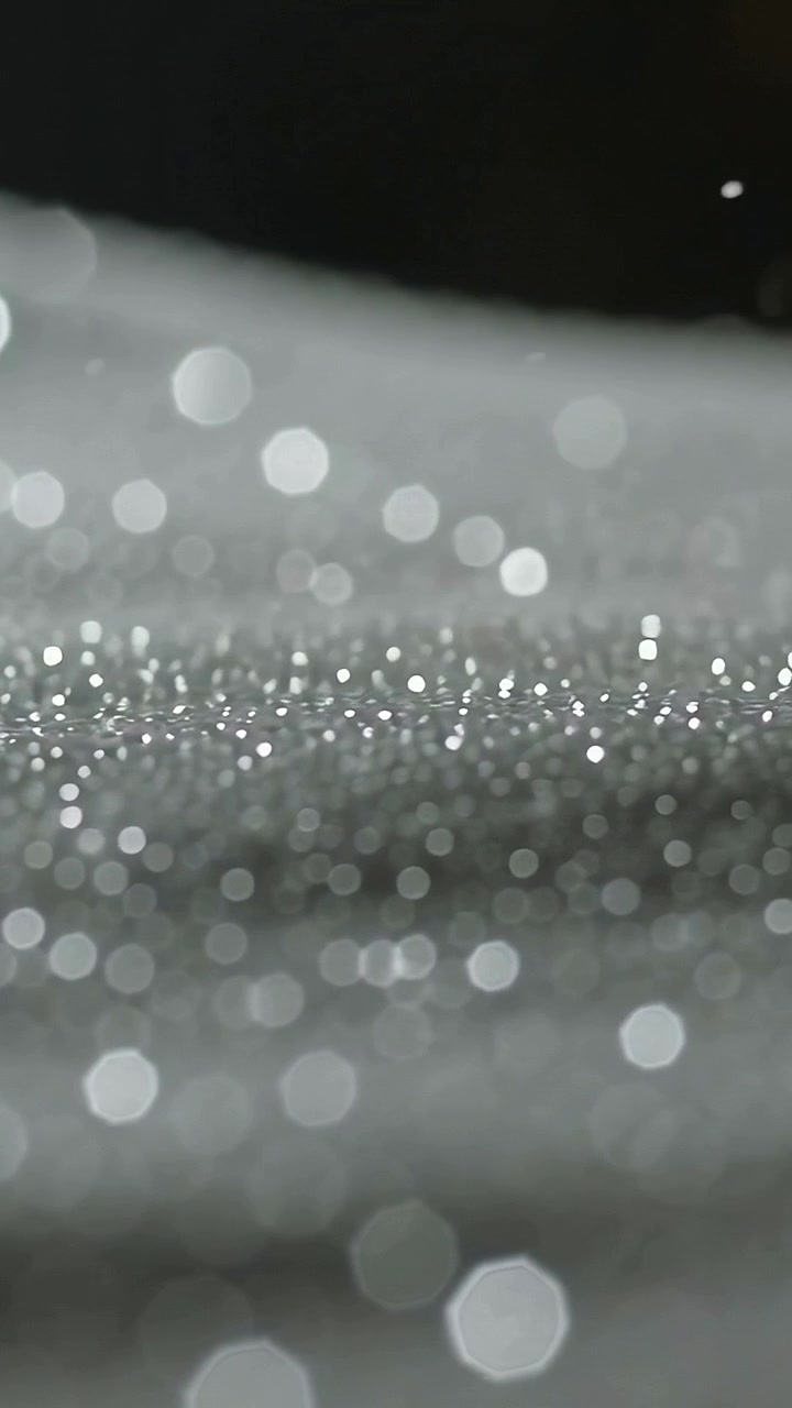 Video verticale: Superficie scintillante che rivela granuli e bokeh in studio mentre la fotocamera sposta la messa a fuoco