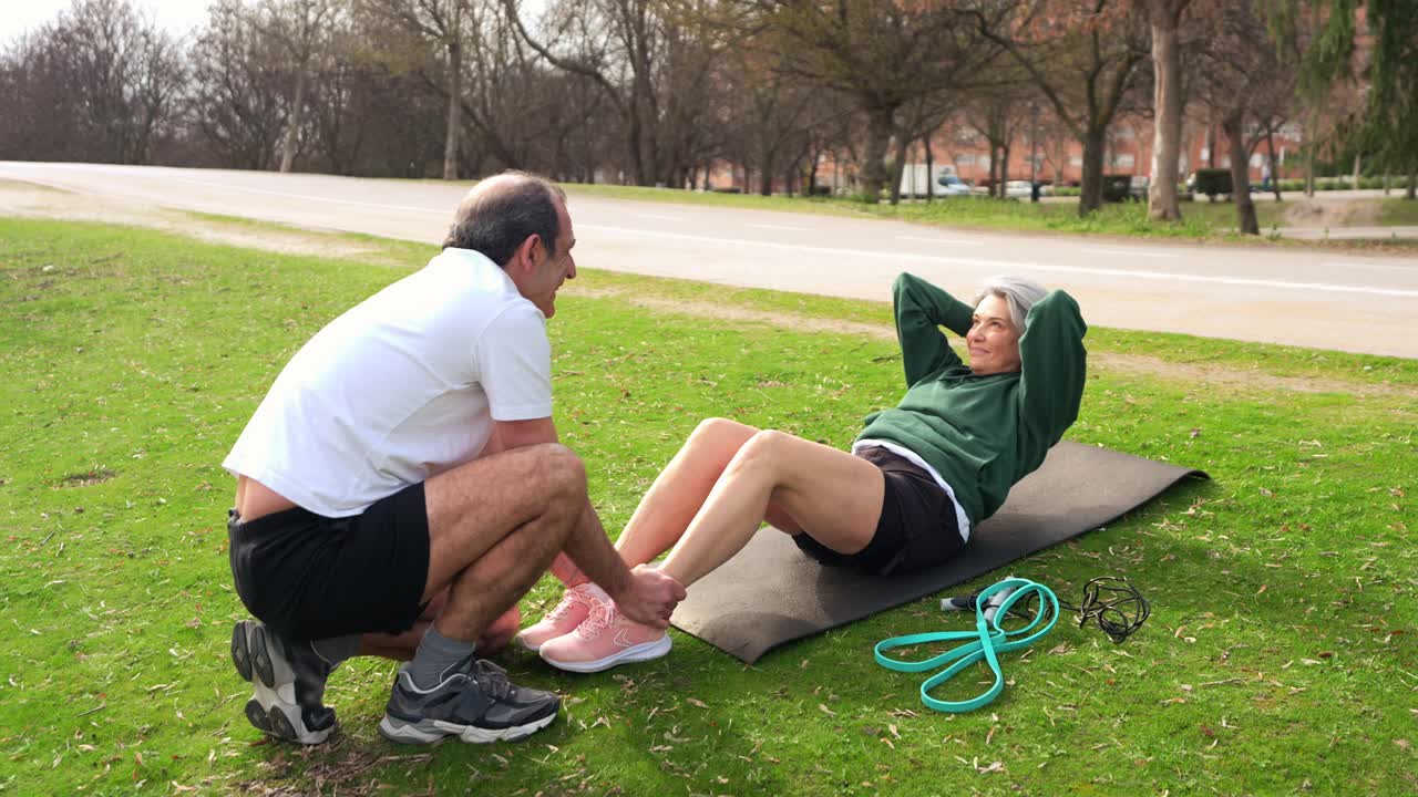Pareja de adultos mayores activos haciendo abdominales en una esterilla de yoga al aire libre