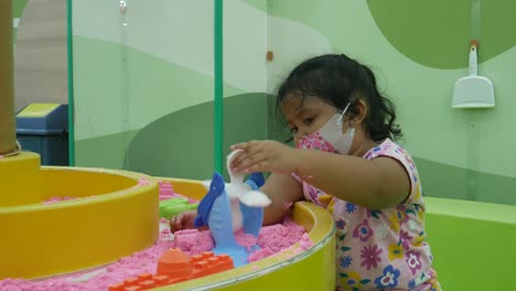 asian little girl playing in the sandbox on the playground in the mall during covid-19 pandemic