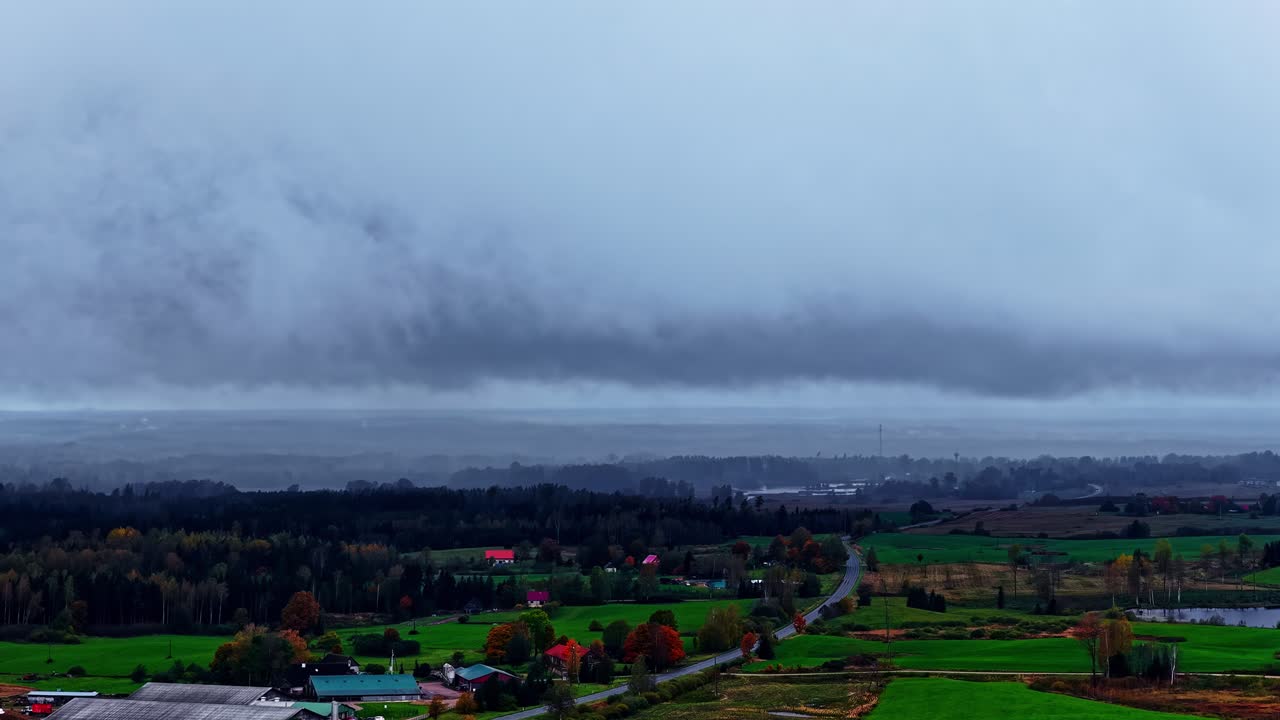 Overcast landscape with distant green fields under dark stormy sky, churning clouds