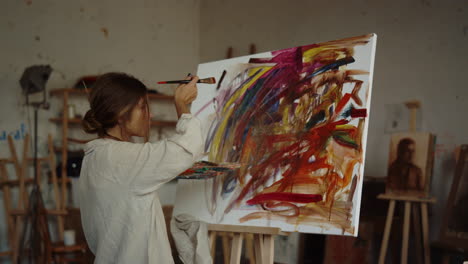 Talented-woman-painting-in-studio.-Inspired-painter-using-oil-paints-indoors.