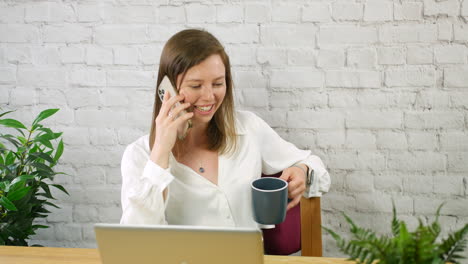 joven mujer de negocios tomando un descanso hablando por teléfono y bebiendo café en una oficina sentada en un escritorio