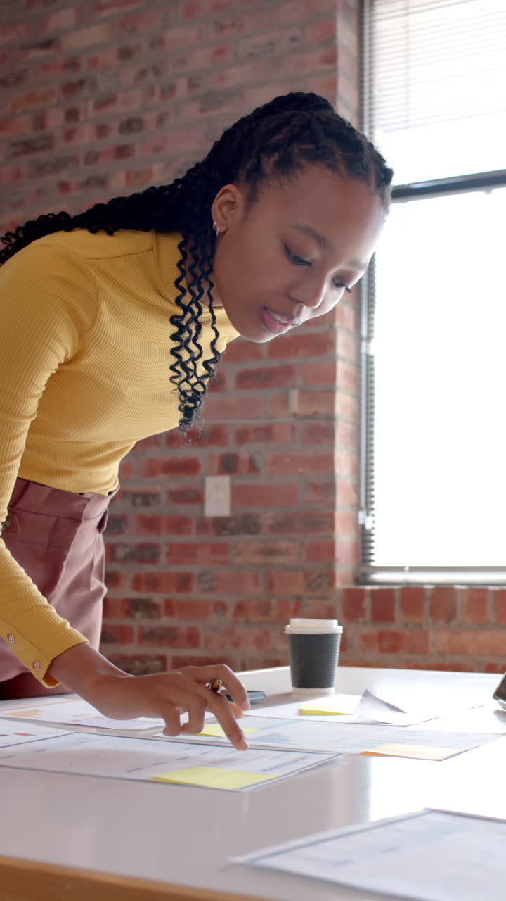 Vertical video of african american casual businesswoman looking at documents in office, slow motion