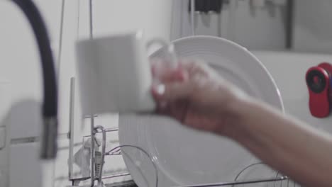 close up, person's arm hanging ceramic cup on drying rack after washing in kitchen sink