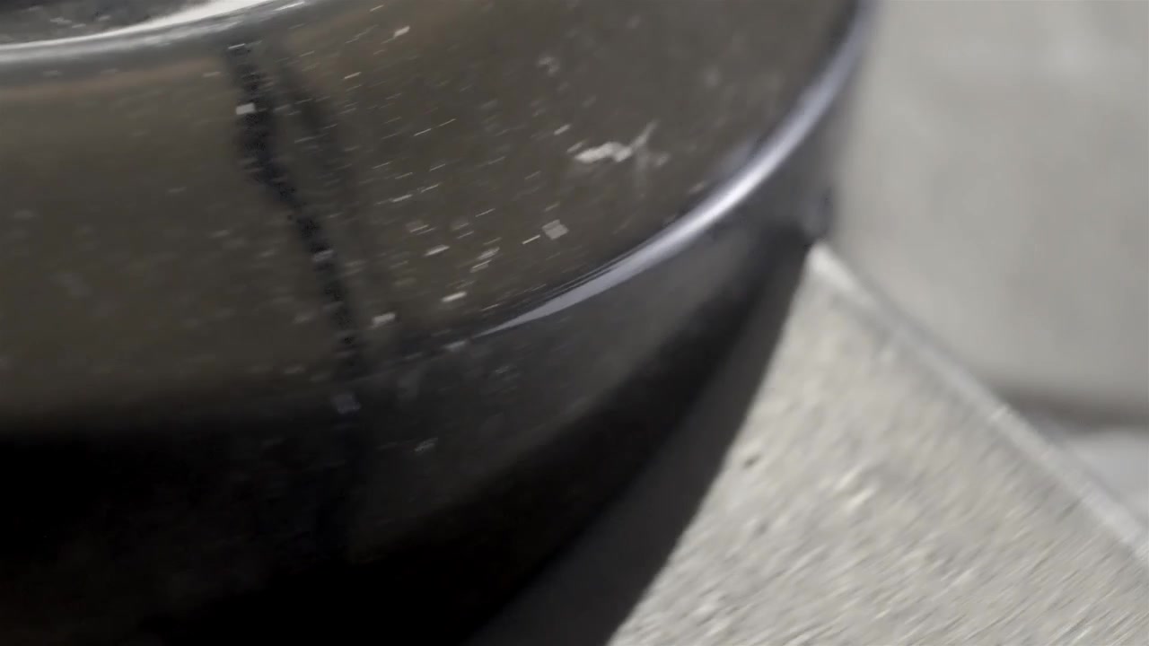 Partículas de polvo cubren un ventilador oscilante negro en primer plano junto a un suelo gris.