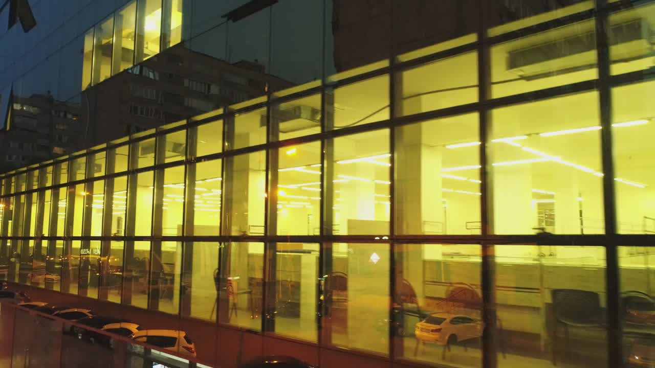 비즈니스 디스트릭트 건물의 4k 외관, 저녁이나 밤에 벽 거울 창문이있는 쇼핑몰, 거울 벽에 도시, 사람, 자동차의 반사, 드론 카메라 이동, 내부에서 일하는 사람들