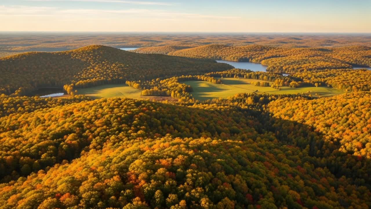 Breathtaking Aerial View of Rolling Hills Covered in Autumn Foliage, Showcasing Vibrant Colors and Serene Lakes Beneath a Warm Sky in the Golden Hour